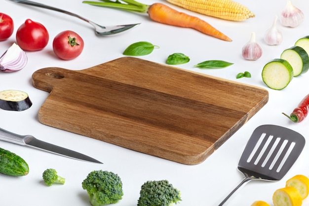 Fondo blanco culinario con verduras y utensilios de metal de tablero de madera