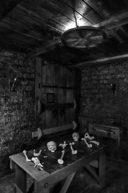 Fondo blanco y negro en el místico interior oscuro de la habitación medieval con mesa de madera con calaveras y huesos