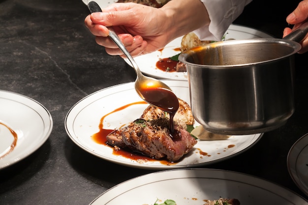 El fondo borroso del chef está vertiendo la salsa en la carne es el plato principal.