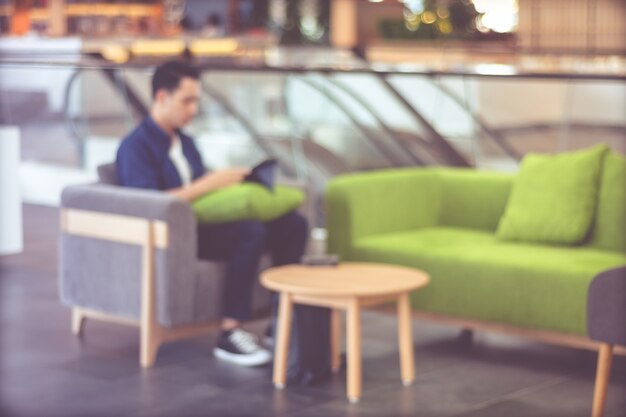 Fondo borroso, hombre joven en estilo casual con tableta mientras está sentado en el sofá en concepto de fondo, negocios, educación y estilo de vida de café