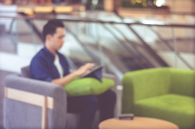 Fondo borroso, hombre joven en estilo casual con tableta mientras está sentado en el sofá en el fondo del café