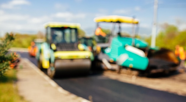 El fondo borroso del sitio de construcción está colocando nuevos trabajadores de la construcción del pavimento de la carretera asfaltada