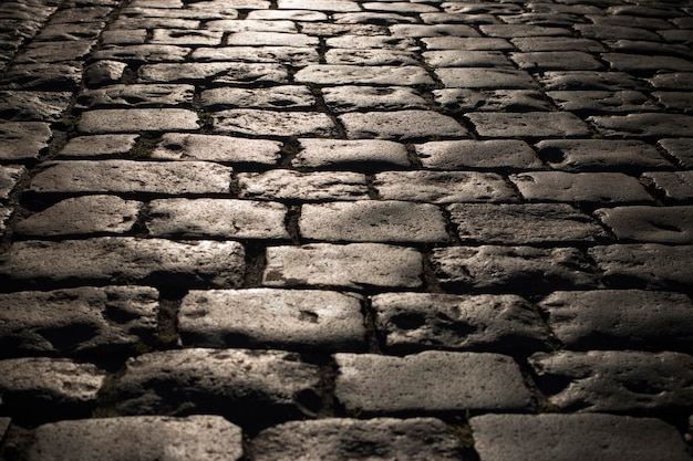 Fondo de camino de piedra adoquinada negra con reflejo de la luz que se ve en la carretera