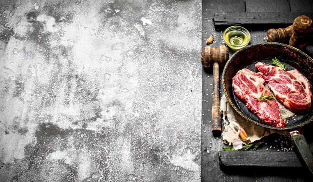 Fondo de carne cruda. Chuleta de cerdo cruda en una sartén vieja con especias y hierbas. Sobre una mesa rústica.