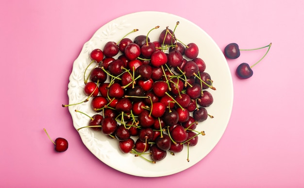 Fondo de cereza. Cereza dulce jugosa roja en un plato blanco sobre un fondo rosa claro. Concepto de comida y bayas jugosas frescas de verano. Foto de alta calidad