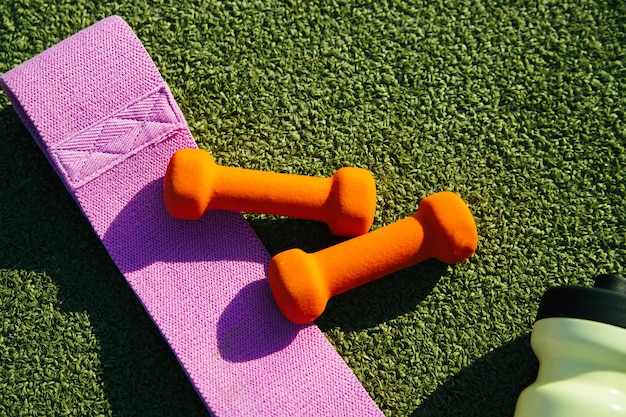 En el fondo de césped artificial hay una esterilla, una botella, una banda elástica de fitness y una esterilla. Equipo deportivo.