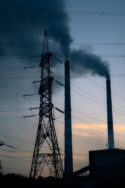 Fondo de cielo de torre de alta tensión, tubo de fábrica con humo sobre él