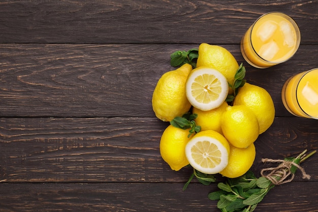 Fondo de cítricos. Vista superior de limones, menta y vasos de limonada con cubitos de hielo. Maqueta para receta de bebida exótica, espacio de copia en madera rústica oscura