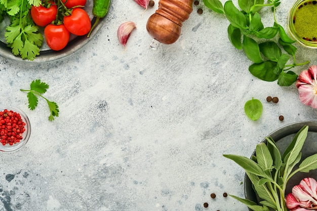 Fondo de cocción de alimentos. Azafrán fresco, ajo, cilantro, albahaca, tomates cherry, pimientos y aceite de oliva, especias, hierbas y verduras en la mesa de pizarra gris claro. Vista superior de los ingredientes alimentarios.