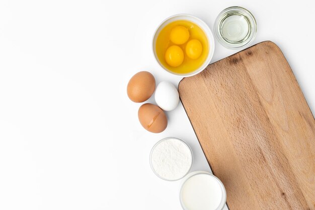 Fondo de cocción con huevos crudos y tabla de cortar de madera en blanco