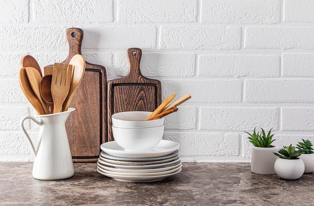 Fondo de cocina elegante con un juego de utensilios blancos y utensilios de cocina de madera sobre una encimera de mármol oscuro contra una pared de ladrillo blanco