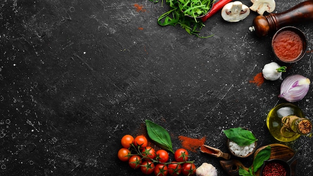 Fondo de cocina: tomates cherry, cebollas, especias y hierbas. Sobre un fondo negro.