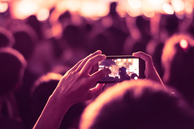 fondo colorido borroso de la mano que sostiene el teléfono inteligente para tomar fotos personas llena en concierto.