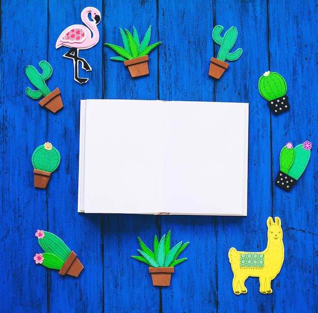 Fondo colorido creativo con elementos dibujados y cortados a mano de moda llama o cactus lama flamenco rosa y libro en blanco para texto Conjunto hecho a mano exótico tropical en la vista superior de la mesa de textura azul