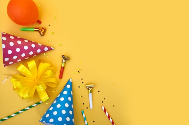 Fondo colorido feliz cumpleaños o fiesta Lay Flat con sombreros de cumpleaños, sopladores, confeti y cintas sobre fondo amarillo. Vista superior con espacio de copia.