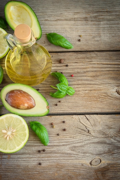 Fondo de comida con aguacate, lima, aceite de oliva y albahaca en viejas tablas desgastadas. Vista superior, espacio para texto.