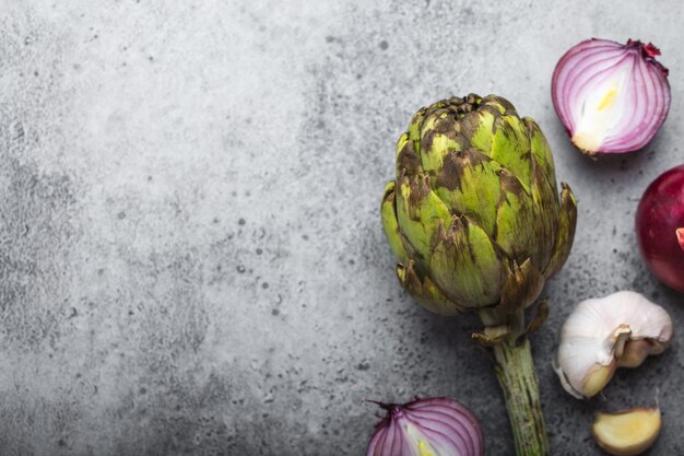 Fondo de comida con espacio libre para texto. Primer plano, vista superior de cebollas crudas cortadas, ajo y alcachofa fresca entera sobre fondo de piedra gris rústico, cocina, comida vegetariana o concepto de alimentación saludable