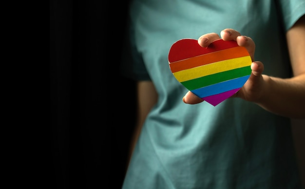 Foto fondo de la comunidad lgbt con foto de espacio de copia. mano de niña con símbolo y bandera de arco iris lgbt en forma de corazón. concepto de tolerancia, derechos de lesbianas y gays