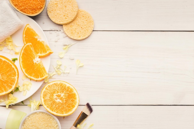 Fondo de cosmetología. Rodajas de naranja, sal marina y esponjas para tratamiento de spa natural sobre fondo de madera blanca. Concepto de cuidado de la piel, vista superior, espacio de copia