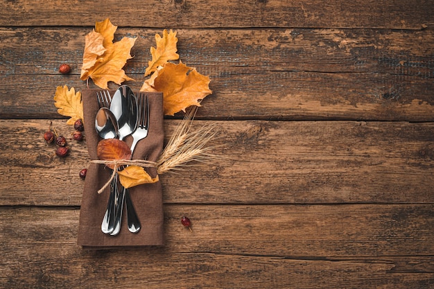 Fondo culinario festivo de otoño con servilleta de cubiertos y hojas de otoño sobre un fondo de madera