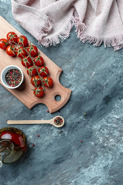 Fondo culinario con tabla de cortar de madera vacía, composición de aceite, chiles, ramita de tomates cherry y especias. imagen vertical. vista superior. lugar para el texto