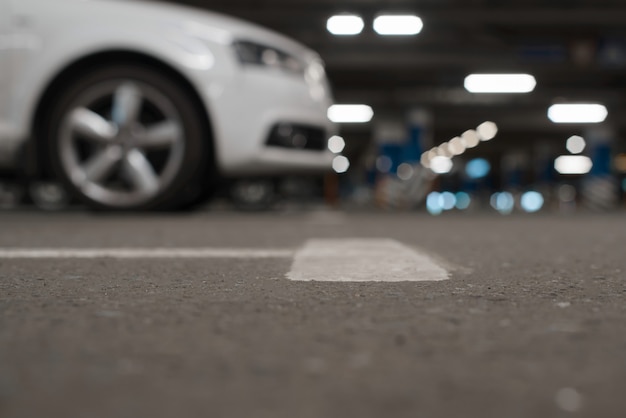 Fondo Defocused de estacionamiento subterráneo, vista de ángulo bajo. Los coches aparcados y las luces se desdibujan, enfoque selectivo en el suelo.