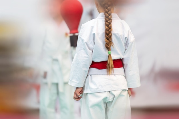 Fondo deportivo para artes marciales con poca profundidad de campo y efecto de desenfoque de movimiento Una chica con una hermosa coleta desde atrás en un kimano blanco con un cinturón rojo