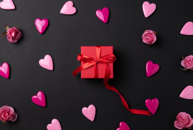 Fondo del día de San Valentín con corazones rojos y regalo sobre fondo negro.