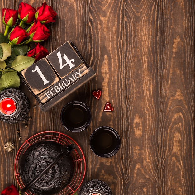 Fondo del día de San Valentín con té verde, tetera negra, velas, rosas y calendario de madera