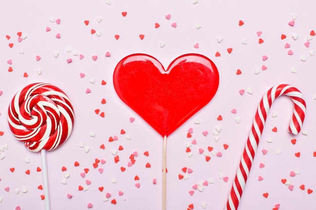 Fondo para el día de San Valentín. Tres piruletas sobre un fondo rosa entre pequeños corazones. Espacio para copiar. Posición plana, vista superior.