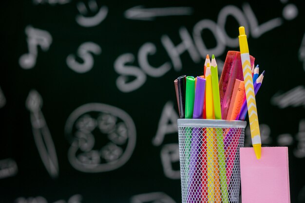 Fondo de escuela con accesorios de papelería. Libros, globo, lápices y diversos suministros de oficina sobre el escritorio sobre un fondo verde pizarra