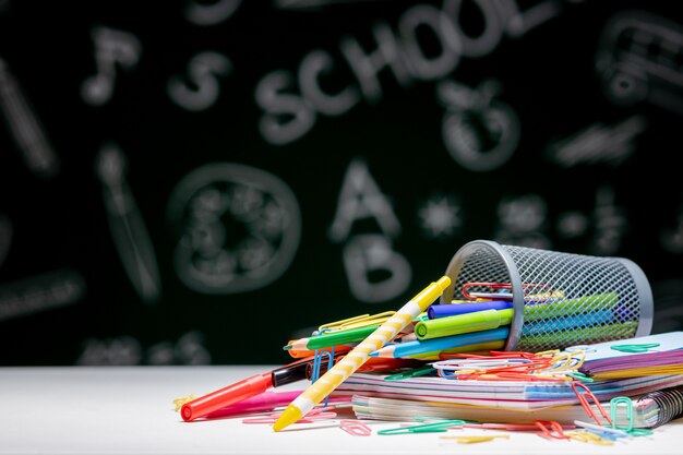 Fondo de escuela con accesorios de papelería. Libros, globo, lápices y diversos suministros de oficina sobre el escritorio sobre un fondo verde pizarra