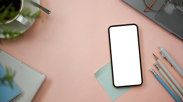 Fondo de espacio de trabajo rosa con maqueta de pantalla en blanco de teléfono inteligente, papelería, computadora portátil y espacio de copia