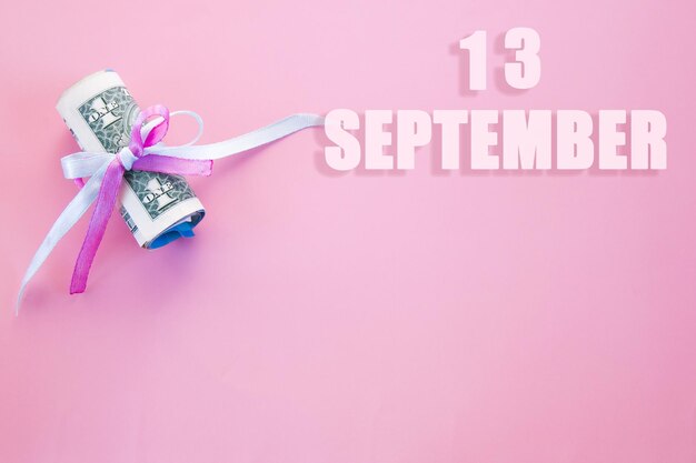 Fondo de fecha de calendario rosa con billetes de dólar enrollados fijados por cinta azul rosa 13 de septiembre