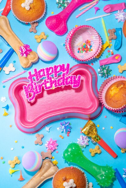 Fondo de feliz cumpleaños para mascotas con diferentes bocadillos para perros y juguetes en forma de hueso para perros cupcakes de cumpleaños con velas de feliz cumpleaños y accesorios Flatlay en la vista superior de fondo azul