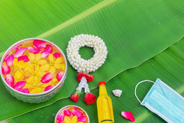 Fondo del Festival Songkran con guirnalda de jazmín Flores en un tazón de agua, perfume y piedra caliza sobre un fondo verde de hoja de plátano húmedo