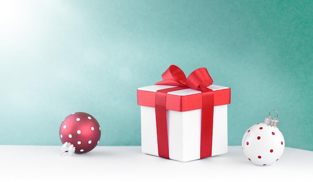 Fondo festivo, caja de regalo blanca con un lazo rojo y dos adornos navideños
