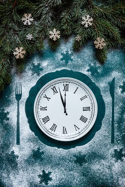 Fondo festivo de Navidad y feliz año nuevo con ramas de abeto, decoración navideña y plato con patrón de reloj que muestra la víspera de año nuevo