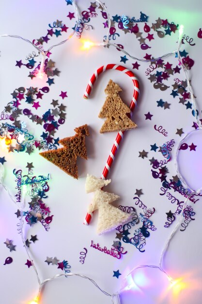Fondo festivo de Navidad o año nuevo. Composición de tarjetas de felicitación con dulces rayados, brillos y abetos hechos de pan. Concepto de vacaciones.
