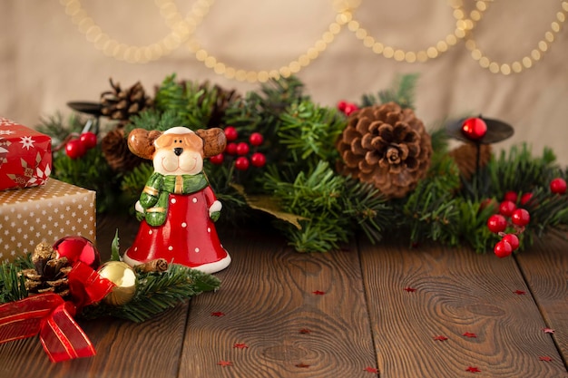 Fondo festivo de Navidad con un reno de juguete vestido como Santa Claus un árbol de Navidad decorado con luces doradas en una mesa de madera espacio de copia de primer plano