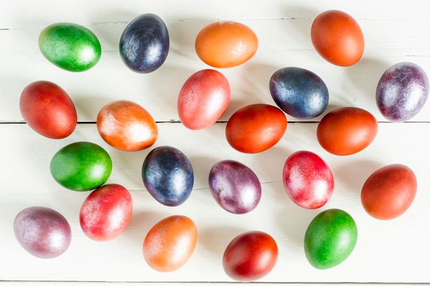 Fondo festivo de Pascua. Huevos pintados multicolores están esparcidos sobre una mesa de madera blanca. vista superior.