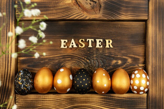 Fondo festivo de Pascua. Vista superior de huevos de Pascua coloreados con pintura dorada e inscripción en Pascua inglesa. Letras de madera sobre fondo de madera oscura.