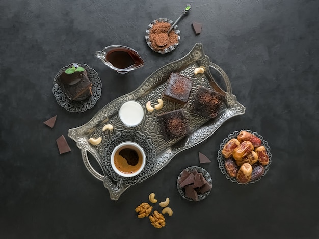 Fondo festivo de Ramadán. Los brownies con dátiles, chocolate negro, leche y café se colocan sobre una superficie negra.