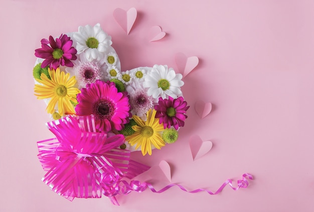 Fondo floral rosa con coloridas margaritas frescas en forma de corazón y corazones de papel y arco de regalo