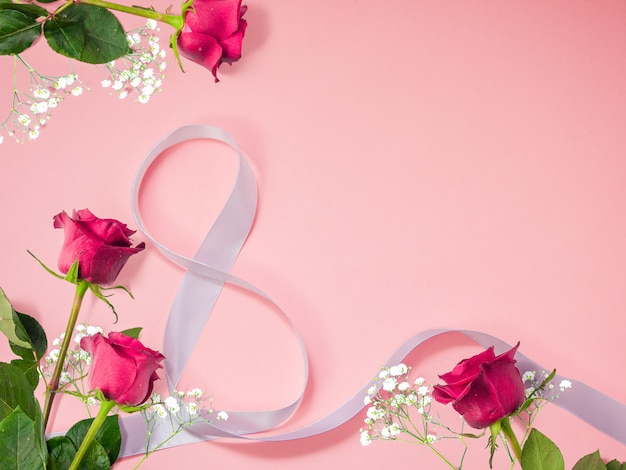 Fondo de flores de rosas con cinta decorativa blanca en forma de 8 para el Día Internacional de la Mujer