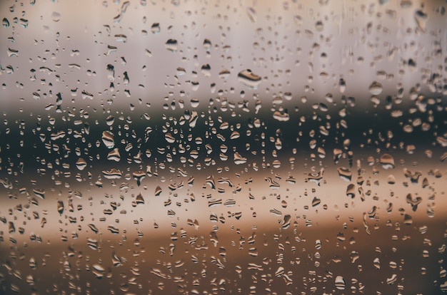 Fondo y fondo de pantalla por gota de lluvia y gotas de agua en el cristal de la ventana.