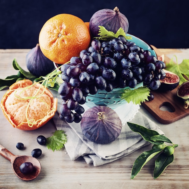 Fondo de frutas de temporada con mandarina, uva azul e higos en cuenco viintage sobre tabla de madera