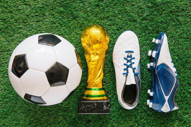 Foto fondo de fútbol en césped con trofeo entre pelota y zapatos