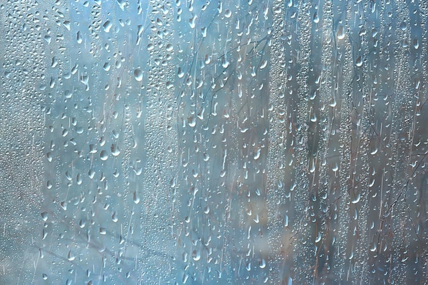 Fondo gotas de vidrio húmedo otoño en el parque / vista del paisaje en el parque de otoño desde una ventana húmeda, el concepto de clima lluvioso en un día de otoño