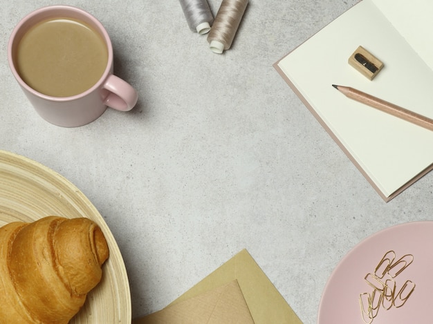 Fondo de granito con taza rosa de café y croissant, notas, sobres, clips